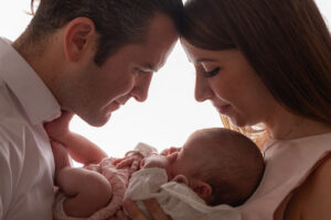 Baby girl being held by mother and father in a close hold looking at baby
