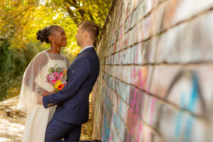 Newly Weds Rob & Lydia, loving embrace leaning against street art graffiti wall. Wedding Photographer Emma Lowe