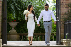 Bride and Groom walking through black metal gates into a walled garden in the sunshine looking at each other