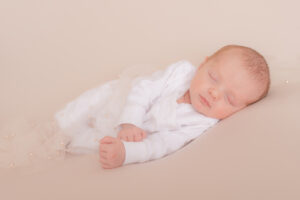White newborn girl clothed in white baby grow with light beaded wrap to give some detailing on image