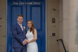 Bride and groom pose on the steps with a bright blue door behind them in a hand hold pose