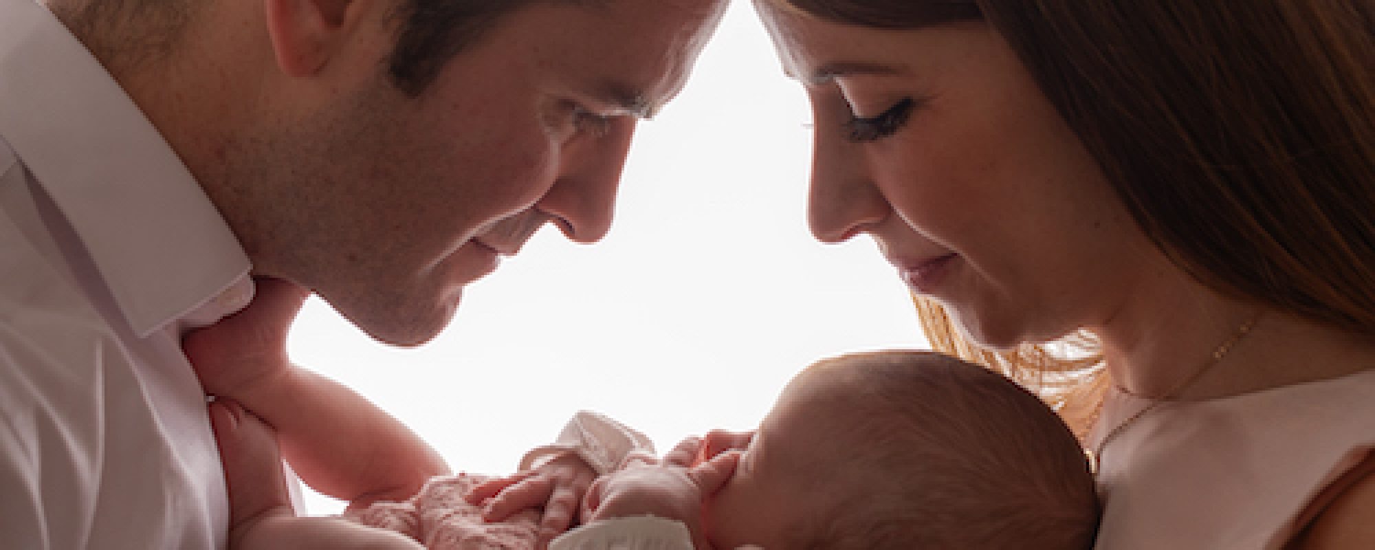 Baby girl being held by mother and father in a close hold looking at baby