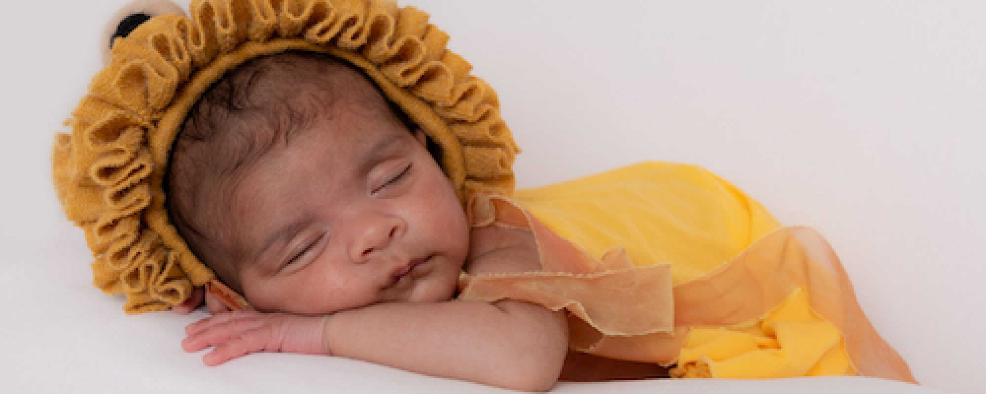 Cute sleeping newborn with yellow wrap and cute lion bonnet