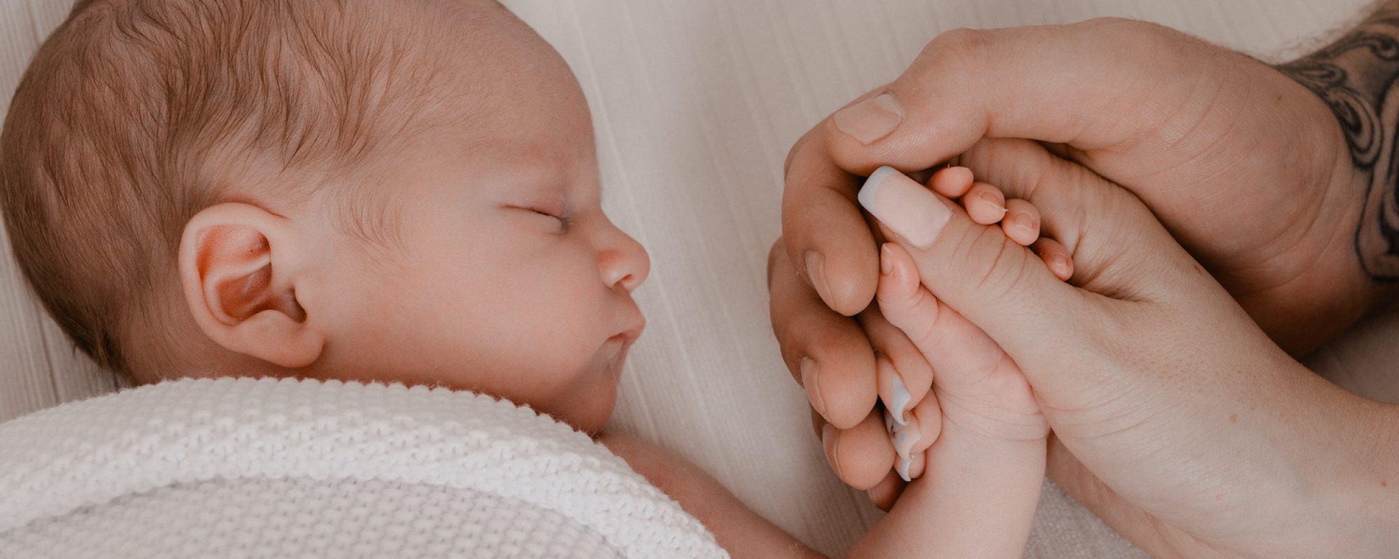Baby with Mother and Father holding the newborns hand